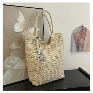 Beige gewebte Stroh Schultertasche mit stylischem Quasten und Perlen Anhänger Detail.