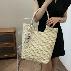 Detailansicht der stilvollen gewebten Stroh-Tote-Bag mit Perlen-Quasten-Anhänger in Beige.