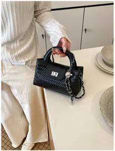 Black woven leather handbag detail, metal lock closure and chain charm decoration.