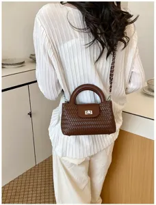 Woven leather top handle handbag detail, brown chain crossbody square bag style scene.