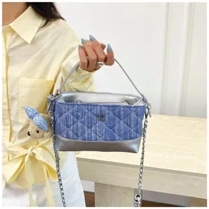 Primo piano della borsa a tracolla in denim trapuntato con catena e ciondolo a forma di orso.
