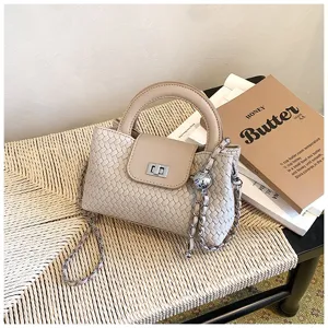 Detail view of a chic beige woven top handle crossbody bag with chain strap and turn-lock closure.