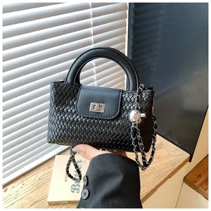 Black woven handbag detail shot, featuring top handle, chic chain strap, and turn-lock closure.