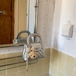 Zilveren gewatteerde handtas in detail, met chique draaisluiting en schattige pluche berenhanger.