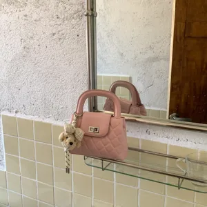 Detail van de roze gewatteerde handtas met metalen draaisluiting en schattige berenhanger op schap.