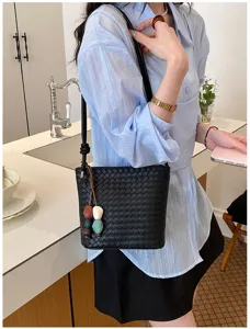 Vue détaillée du sac seau tressé noir mettant en valeur sa texture, sa bandoulière et ses charms.
