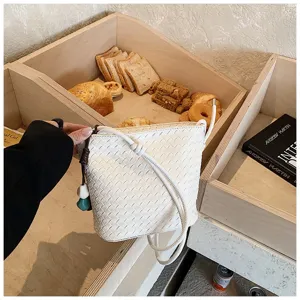 Détail de sac seau tressé blanc, sac bandoulière élégant en cuir avec poignée nouée.