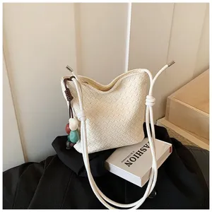 Gros-plan sur les détails d'un sac bandoulière en cuir tressé blanc avec pendentif perlé.