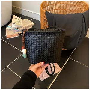 Sac seau en cuir tissé noir détail avec bandoulière élégante et charmant pendentif chic.