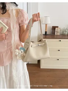 Close-up view of elegant beige leather bucket bag with metal lock and cute bear charm detail.