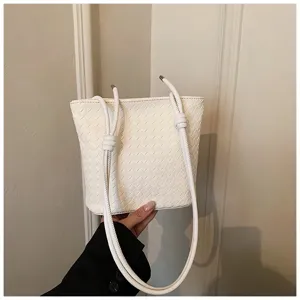 Gros plan sur le sac seau tressé blanc, bandoulière nouée élégante et design minimaliste.