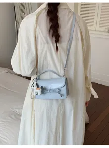 Vista detallada de un bolso cruzado azul claro para mujer con un lindo lazo y dije de caballo.