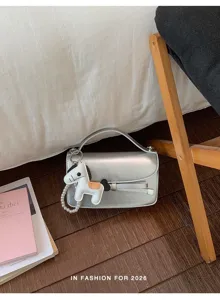 Detalle de bolso metalizado plateado con lazo elegante y dije de poni, foto de estilo.