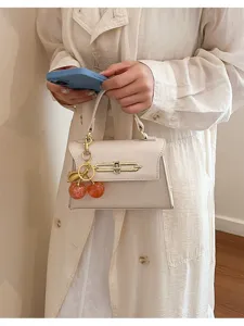 Detailansicht der stilvollen beigen Henkeltasche mit süßem Kirschanhänger und Metallverschluss.