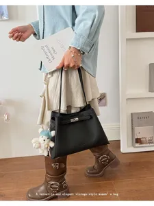 Detailed view of stylish black leather tote bag with metal turn-lock and cute bear pendant.