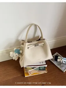 Close-up detail of the elegant beige handbag with turn-lock closure and cute bear charm.