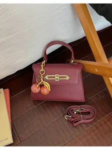 Dunkelrote Leder Handtasche mit goldenem Schloss und niedlichem Kirsch Anhänger für Damen elegant.