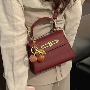 Elegante bordeauxrote Henkeltasche aus Leder mit Metallschloss und süßem Kirsch-Anhänger.