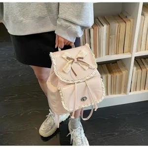 Close-up of pink bow lace backpack held by a model in front of a bookshelf.