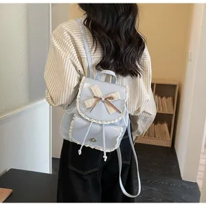 Detail view of a light blue backpack with elegant lace trim and bow detail on a model