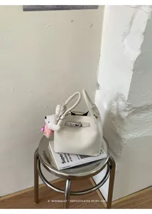 Vista detallada del elegante bolso cubo de cuero blanco con colgante de conejito.