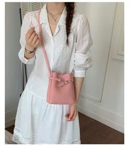 Gros plan détaillé d'un sac seau chic en cuir rose porté avec une robe blanche élégante.