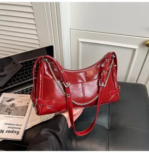 Dettaglio borsa a spalla rossa in pelle verniciata con eleganti cinturini con fibbia e catena.