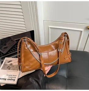 Primo piano della borsa a spalla in pelle marrone rétro con catena metallica e fibbia elegante.