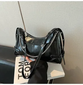 Vista di dettaglio della borsa a spalla in pelle verniciata nera con eleganti catene e fibbie.
