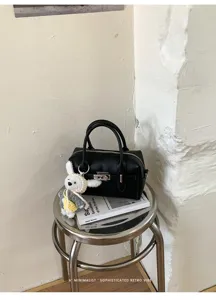 Schwarze Bowling-Handtasche aus Litschistruktur im Detail mit Schloss und niedlichem Anhänger.