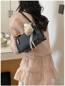 Detailansicht der stylischen schwarzen Schultertasche mit Plüsch-Anhänger und Nieten-Akzenten.
