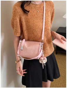 Schicke rosa Umhängetasche mit strukturiertem Stoff, Metallverschluss und Plüsch-Anhänger.