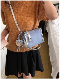 Detailansicht einer blauen Jeans-Umhängetasche mit silbernen Riemen und Bären-Anhänger.