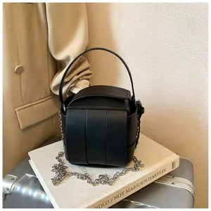 Detailaufnahme einer schwarzen strukturierten Tasche mit Metallkette und feinem Griff.
