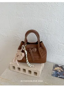 Nahaufnahme der braunen gewebten Ledertasche mit süßem Bären-Schlüsselanhänger und Gürtel.