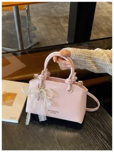 Detailansicht der rosa Handtasche mit elegantem Spitzen-Perlen-Anhänger und Knotengriff.