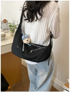 Detaillierte Aufnahme einer schwarzen Schultertasche mit niedlichem Bärenanhänger am Model.