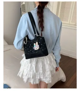 Detail view of a black tote bag with floral print and cute rabbit pendant worn on shoulder.