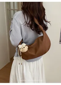 Nahaufnahme des braunen Leder-Hobo-Bags mit süßem Plüsch-Bären-Anhänger als modisches Detail.