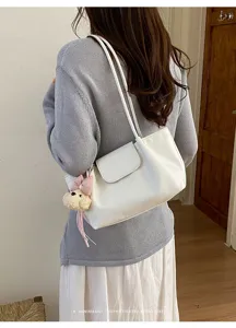 Vista detallada del bolso de hombro de cuero blanco con colgante de peluche estilo retro.