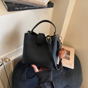 Détail de sac seau noir élégant avec texture grainée, poignée et charm d'ours mignon.