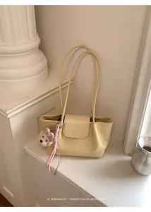 Primer plano detallado del bolso de hombro amarillo claro minimalista con llavero de oso.