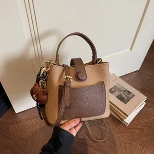 Détail de sac seau bicolore chic, sac bandoulière en cuir PU avec charm d'ours élégant.