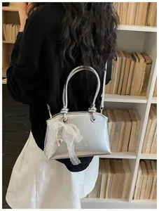 Silberne Metallic-Handtasche Detail mit Spitzen-Perlen-Schleife und Metallgriff.