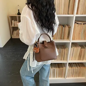Élégant sac seau en cuir marron avec joli pendentif ours porté devant une bibliothèque.