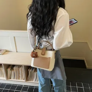 Détail de petit sac seau chic en cuir bicolore avec un charmant pendentif ours en peluche.