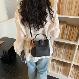 Élégant sac seau en cuir noir pour femme, doté d'une poignée, d'une bandoulière et d'un joli charm d'ours.
