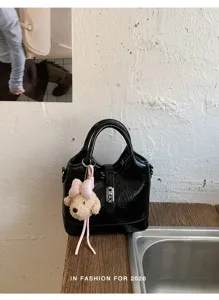 Détail de sac seau en cuir froissé noir avec charmant porte-clés ours et fermoir en métal.
