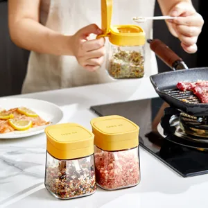 Bote de especias de vidrio transparente con tapa amarilla, ideal para sal y condimentos de cocina.