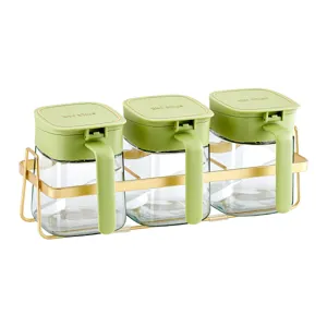 Juego de especieros de cristal con 3 tarros, tapas verdes y soporte dorado de cocina.